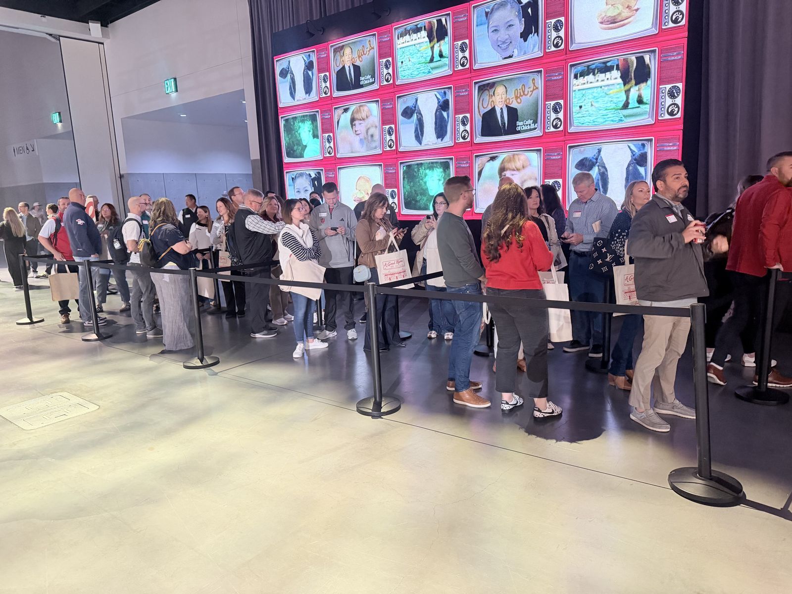 Long line of event guests holding canvas totes while waiting for a live personalization station