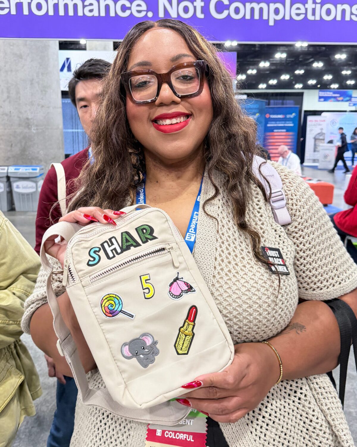 Guest smiling and holding a cream sling bag personalized with SHAR chenille letter patches at a live event